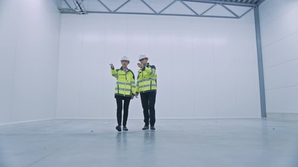 Poster - Two Engineers Talking, Walking Across Empty Factory Floor, inspecting, Planning Where All the Machinery Would go. Professionals Industrial Designers Strategizing about New Manufacturing Plant Design