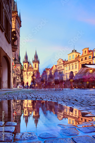 Cuadros en Lienzo St Mary Tyn Church in Prague with reflection in a pool of water after Summer rain with tourists walking by towards Old Town Square