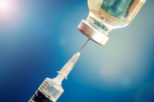 A Bottle With Vaccine And Syringe In Front Of Blue Background. Medicine, Science And Healthcare Concept