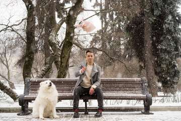 Boy friend with a bouquet and a white dog of pink flowers hydrangea waiting for a date with his girl friend on a bench in a park outdoors on Valentine`s day.