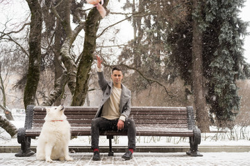 Boy friend with a bouquet and a white dog of pink flowers hydrangea waiting for a date with his girl friend on a bench in a park outdoors on Valentine`s day.