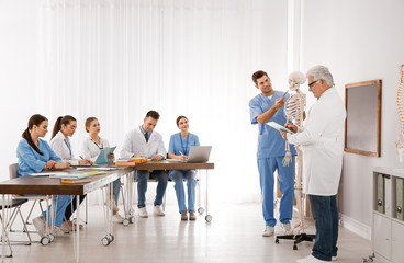 Canvas Print - Medical students and professor studying human skeleton anatomy in classroom