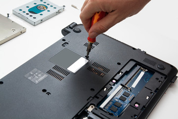 Laptop repair. A wizard with a screwdriver disassembles the laptop case for parts to replace parts and repair.