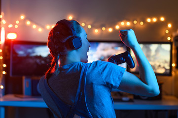 Wall Mural - Gamer or streamer girl at home in a dark room with a gamepad playing video games with friends online. Young man sits in front of a monitor