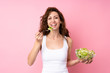 © luismolinero - Young woman with curly hair holding a salad over isolated pink background