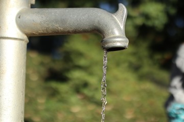 Sticker - Closeup landscape shot of a gray faucet dripping water with a blurred in the background