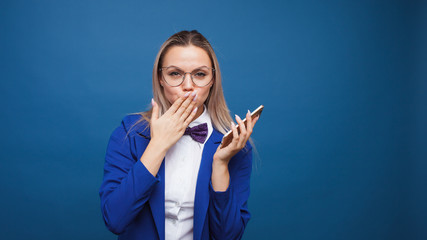 Wall Mural - Cute and funny businesswoman in a stylish blue jacket and bow tie uses a smartphone.