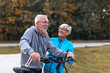 Older couple in park, he is with bicycle and she walk beside and talking