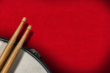 Close-up of two wooden drumsticks and an old metallic snare drum on a red velvet background with copy space. Percussion instrument