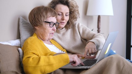 Granddaughter Helping Grandmother With Laptop Lying In Bed. Technology, People And Generation Concept.