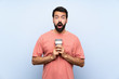 Young man with beard holding a take away coffee over isolated blue background with surprise facial expression