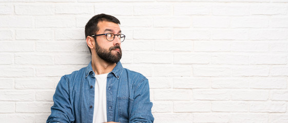 Wall Mural - Handsome man with beard over white brick wall with confuse face expression