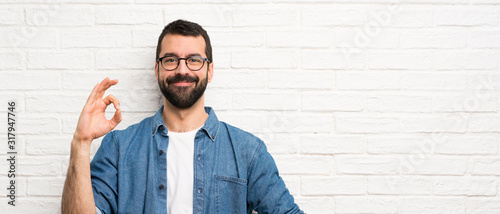 Fotografía Handsome man with beard over white brick wall showing ok sign with fingers