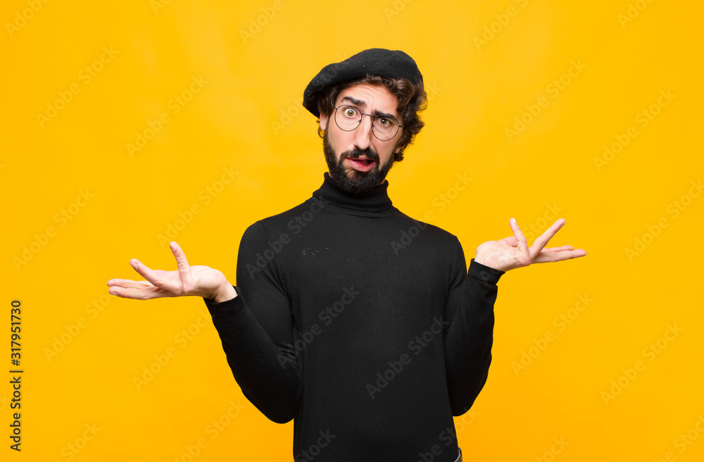 young french artist man shrugging with a dumb, crazy, confused, puzzled expression, feeling annoyed and clueless against orange wall - obrazy, fototapety, plakaty 
