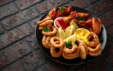 Wall Mural - Sticky glazed chicken wings and deep fried battered onion rings served with lemon wedges, tomato ketchup and mustard. Greasy, fast food concept