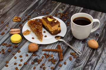 Cup of coffee and two slices of cake and macaroons on the plate on wooden table