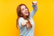 canvas print picture - Teenager redhead girl over isolated yellow background points finger at you while smiling