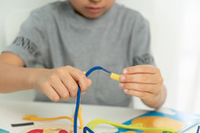 Close Up Of Child Hands Playing With Lace Or Rope And Pasta. Development Of Fine Motor Skills. Early Education, Montessori Method. Cognitive Skills,