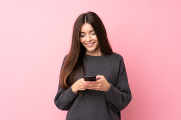 Wall Mural - Young woman over isolated pink background sending a message with the mobile