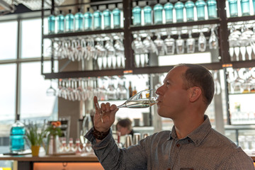 A young man drinks sparkling wine in a light-flooded bar. Concept: lifestyle or alcohol abuse