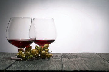 Glasses with red dry wine. A bouquet of dried roses. Stand on wooden boards. Shot in backlight.