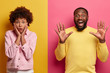 © wayhome.studio  - Human face expressions and emotions concept. Studio shot of surprised Afro American woman holds palms on cheeks, wears pink jacket, funny guy laughs at something with raised palms. Two colored wall