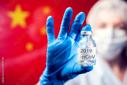 A doctor in blue medical gloves and mask holding an ampula with vaccine in front of flag of China Canvas Print