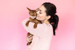 Girl in a dress with a Bengal cat on a pink background in front of camera