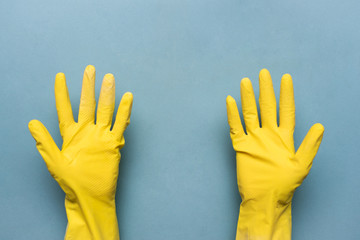 Wall Mural - Female hand in yellow glove is holding copy space on blue background.