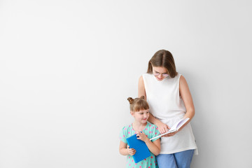 Poster - Beautiful young woman and her little daughter with books on light background