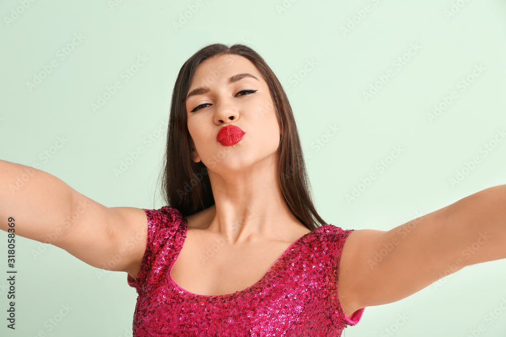 Beautiful young woman taking selfie on color background