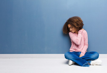 african american little girl feeling tired, stressed, anxious, frustrated and depressed, suffering with back or neck pain sitting on the floor