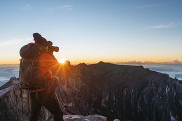 Wall Mural - a man with backpack taking photo over the clouds in sunrise moment on kota kinabalu summit in malays