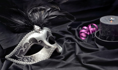 carnival mask on dark satin fabric background with a candle and pink ribbon