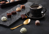 Luxury Chocolate candies selection with cup of black coffee and golden spoon on black marble board and dark table background.