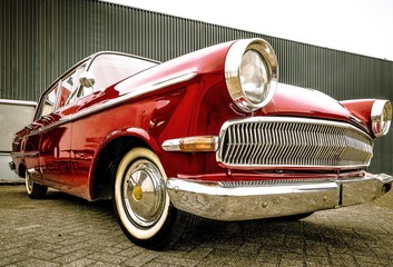 Canvas Print - Low angle shot of a red car standing in front of a grey garage during daytime