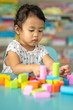 © tienuskin - Cute little girl playing with multicolor wooden building blocks on blue table.