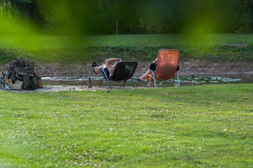 two people relax in sun loungers in the garden by the pond, next to the fireplace material, lawn with flowering clover in the foreground