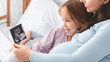 © Prostock-studio - Cute little girl looking at ultrasound scan showed by mom