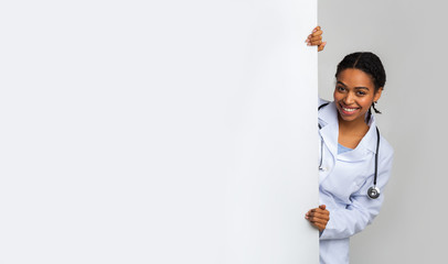 Wall Mural - Young female medical intern looking out of behing white advertising board