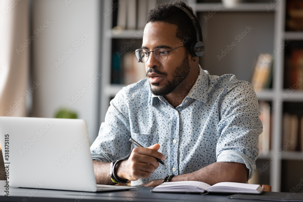 Focused african businessman wear headphones study online watching webinar - obrazy, fototapety, plakaty 