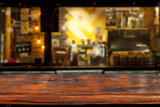 Fototapeta Londyn - Wooden board on a background of bottles with alcohol. Old bar counter as layout for design. Workpiece for design. Empty place to advertise products. Blurred interior of the bar in the background.