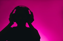 Silhouette Of A Female In Headphones Isolated On A Pink Background. Music Concept 