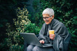 © bnenin - Smiling senior businesswoman using laptop in the garden, portrait.