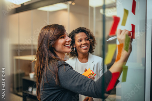 Fotomural Smiling businesswoman brainstorming with adhesive notes on a glass wall in the office