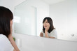 Young asian woman suffering from toothache, tooth decay or sensitivity while she brushing her teeth in front of the bathroom mirror. Dental health care concept.