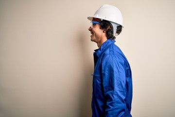 Young constructor man wearing uniform and security helmet over isolated white background looking to side, relax profile pose with natural face with confident smile.