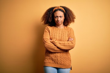 Young african american woman with afro hair wearing casual sweater over yellow background skeptic and nervous, disapproving expression on face with crossed arms. Negative person.