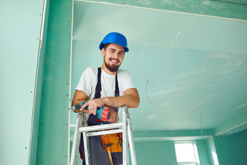 A builder standing on a ladder installs drywall at a construction site