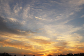 Sunset over the village. Dramatic coloring of the evening sky with cumulus clouds. Golden range of colors of nature. Prediction of changing weather conditions. Romantic mood. Black silhouette